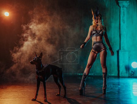 Foto de Elegante mujer sexy en traje y máscara posando con perro doberman - Imagen libre de derechos