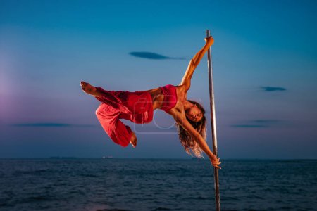 Photo for Young woman pole dancing on sea and sky background at twilight - Royalty Free Image