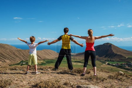 Photo for Happy family of hikers stands on top of a mountain with their arms spread out to the sides - Royalty Free Image