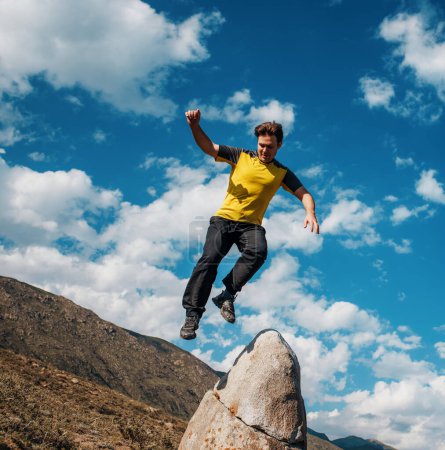 Foto de Joven saltando desde una gran piedra sobre el fondo de las montañas - Imagen libre de derechos