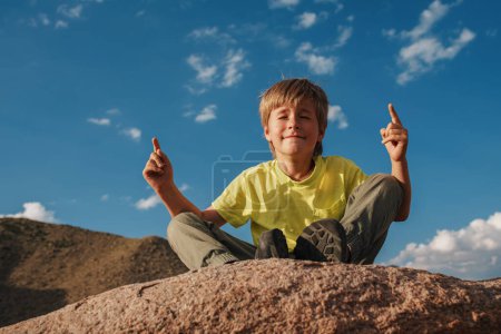 Téléchargez les photos : Garçon assis en méditation pose sur le rocher dans les montagnes - en image libre de droit