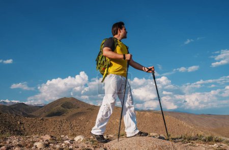 Foto de Hombre excursionista con mochila y bastones de trekking de pie en las montañas - Imagen libre de derechos