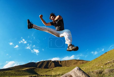 Photo for Handsome athletic young man jumping on mountains background - Royalty Free Image