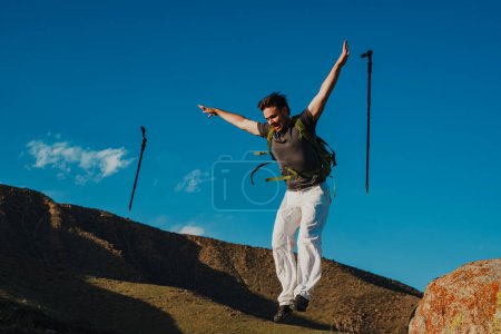 Photo for Hiker with backpack and trekking poles jumps off a cliff - Royalty Free Image