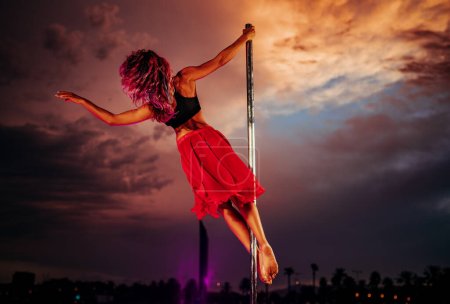 Photo for Young beautiful woman pole dancing on twilight sky and city silhouettes background - Royalty Free Image