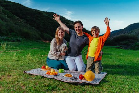 Téléchargez les photos : Joyeux famille avec chien lors d'un pique-nique en montagne - en image libre de droit