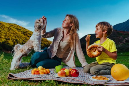 Photo for Happy mom and son feeding their dog at picnic in the mountains - Royalty Free Image