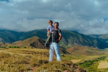 Photo for Happy boy sitting in his father's arms on mountains background - Royalty Free Image