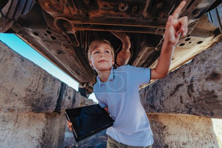 Foto de Lindo niño mecánico automotriz de pie debajo de la parte inferior del coche con la tableta - Imagen libre de derechos