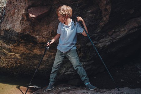 Téléchargez les photos : Garçon randonneur avec bâtons de trekking se tient dans la grotte - en image libre de droit