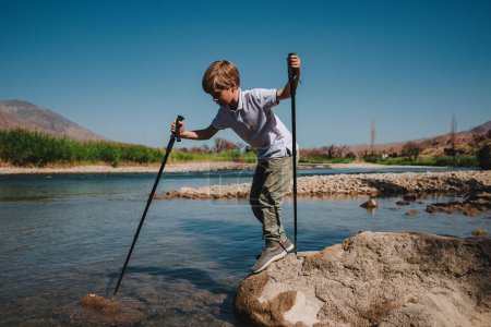Foto de Niño con bastones de trekking comprueba la profundidad del río de montaña - Imagen libre de derechos