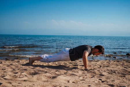 Téléchargez les photos : Sport jeune homme faisant push-ups sur la plage - en image libre de droit