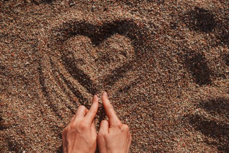 Téléchargez les photos : Mains de femme dessinant la forme du cœur dans le sable le jour d'été - en image libre de droit