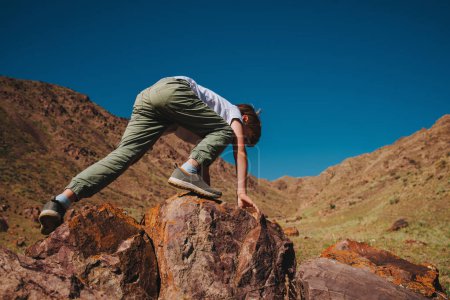 Téléchargez les photos : Garçon escalade sur gros rocher dans les montagnes - en image libre de droit