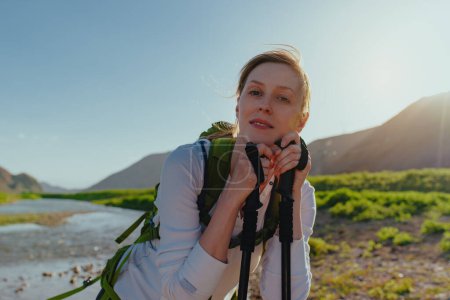 Téléchargez les photos : Portrait de jeune touriste avec sac à dos et bâtons de trekking près de la rivière de montagne - en image libre de droit