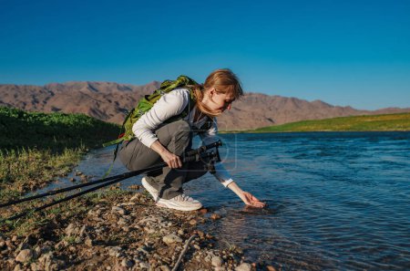 Téléchargez les photos : Jeune femme touriste toucher l'eau dans la rivière de montagne avec sa main - en image libre de droit