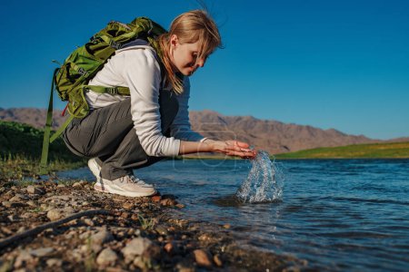 Téléchargez les photos : Jeune femme touriste avec éclaboussure d'eau propre dans la rivière de montagne - en image libre de droit
