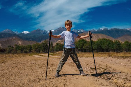 Téléchargez les photos : Garçon voyageur avec bâtons de trekking se tient sur la route des montagnes à l'été - en image libre de droit