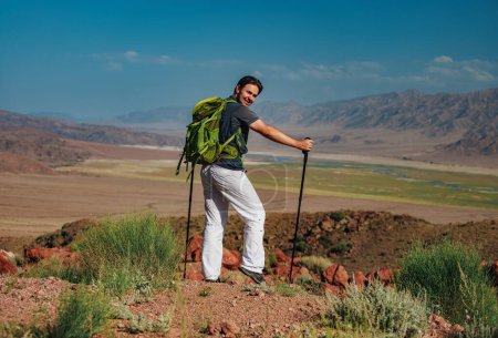 Foto de Senderista en la cima de la montaña con mochila y bastones de trekking vueltos hacia atrás - Imagen libre de derechos