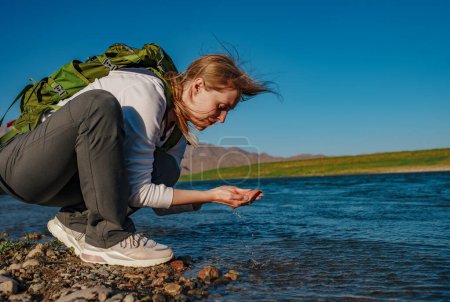 Téléchargez les photos : Jeune femme touriste ramasse l'eau dans la rivière de montagne - en image libre de droit