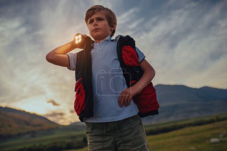 Téléchargez les photos : Sauveteur garçon sérieux avec lampe de poche debout au coucher du soleil montagnes fond - en image libre de droit