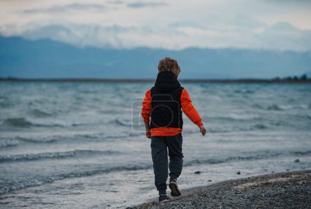 Photo for Boy traveler walking along lake shore in cool weather - Royalty Free Image