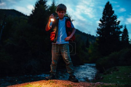 Foto de Niño turista con linterna de pie en el parque natural en el crepúsculo - Imagen libre de derechos