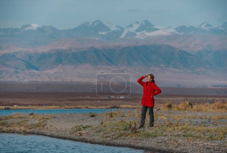 Téléchargez les photos : Femme touriste se tient sur le rivage du lac sur fond de montagnes et regardant loin - en image libre de droit
