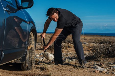 Photo for Young man throws rocks from under the wheel of stuck car - Royalty Free Image