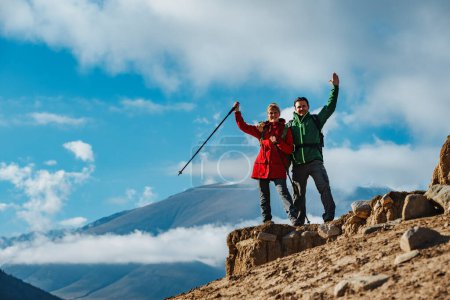 Photo for Happy couple of tourists standing on top of the mountain and waving hands - Royalty Free Image