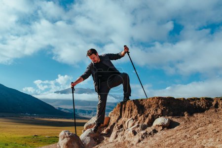 Téléchargez les photos : Homme randonneur avec bâtons de trekking descendant des rochers - en image libre de droit