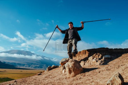 Téléchargez les photos : Homme randonneur saute du haut de la roche sur fond de ciel - en image libre de droit
