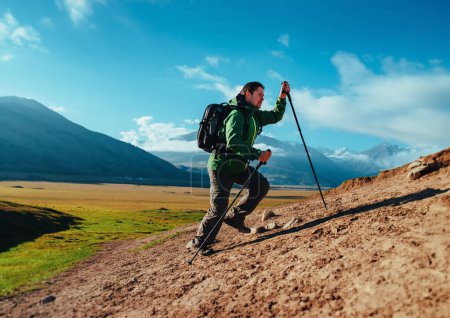 Photo for Man hiker with trekking poles and backpack climbing up the mountain - Royalty Free Image