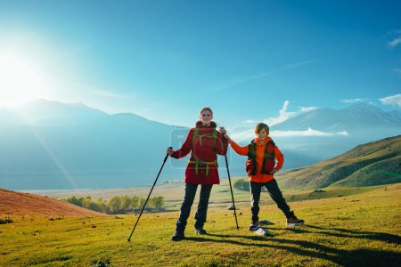Téléchargez les photos : Jeune touriste avec son fils debout dans la vallée verdoyante de montagne à la journée ensoleillée - en image libre de droit