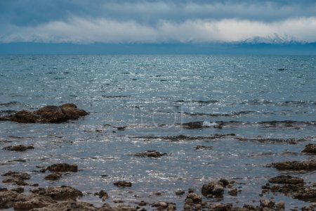 Foto de Orilla rocosa del lago Issyk-Kul con montañas y nubes, Kirguistán - Imagen libre de derechos