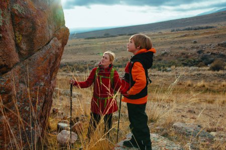 Foto de Joven turista con su hijo de pie cerca de una enorme roca en las montañas - Imagen libre de derechos