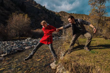 Foto de El hombre ayuda a las jóvenes excursionistas a no caer al arroyo de montaña - Imagen libre de derechos
