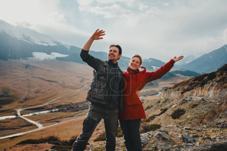 Foto de Feliz pareja de turistas saludando las manos en el valle de la montaña en otoño - Imagen libre de derechos