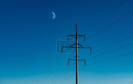 Foto de Líneas eléctricas sobre fondo cielo azul con luna grande - Imagen libre de derechos