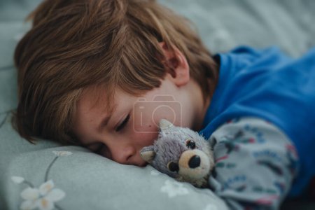Téléchargez les photos : Petit garçon avec jouet dormant dans son lit tôt le matin - en image libre de droit