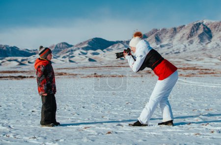 Téléchargez les photos : Femme touriste prend une photo de son fils dans les montagnes en hiver - en image libre de droit