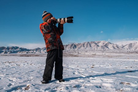 Téléchargez les photos : Garçon avec caméra professionnelle sur fond de montagne en hiver - en image libre de droit