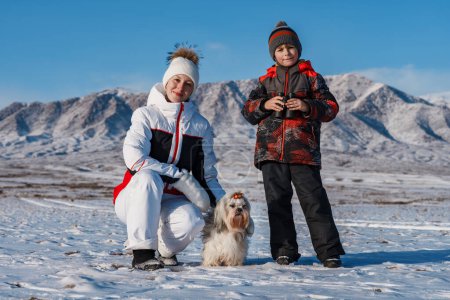 Téléchargez les photos : Mère, fils et chien shih tzu sur fond de montagnes d'hiver - en image libre de droit