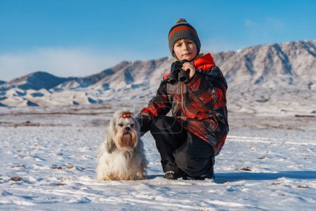 Foto de Niño con prismáticos y perro shih tzu posando sobre el fondo de las montañas en invierno - Imagen libre de derechos