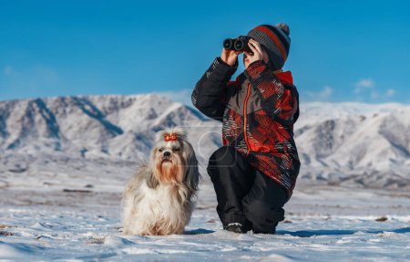 Foto de Niño con prismáticos y shih tzu perro posando en las montañas de fondo en invierno - Imagen libre de derechos