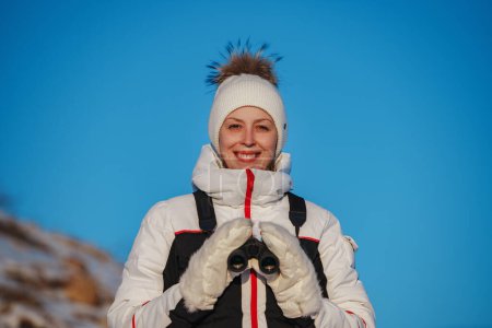 Photo for Young smiling woman tourist with binoculars on mountains background in winter day - Royalty Free Image