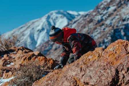Foto de Niño escalando en la roca grande en las montañas en invierno - Imagen libre de derechos