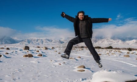 Foto de Joven hombre feliz saltando sobre las montañas de fondo en invierno - Imagen libre de derechos