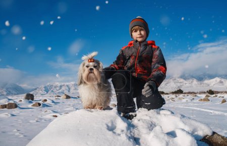 Téléchargez les photos : Garçon avec shih tzu chien portrait d'hiver sur fond de montagnes - en image libre de droit