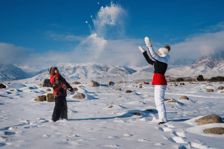 Photo for Young woman and son playing snowballs on mountains background in winter - Royalty Free Image